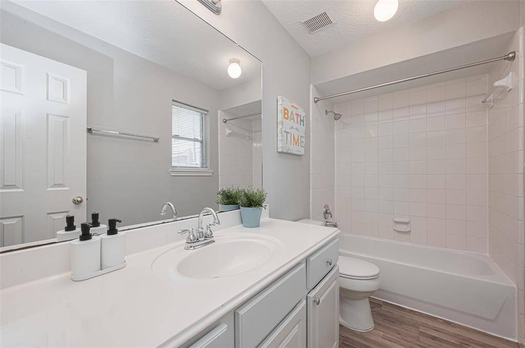 The bathrooms offers a fresh and bright feel with its white countertops, light cabinetry, and wood-look flooring. The spacious mirror enhances the natural light in the room.