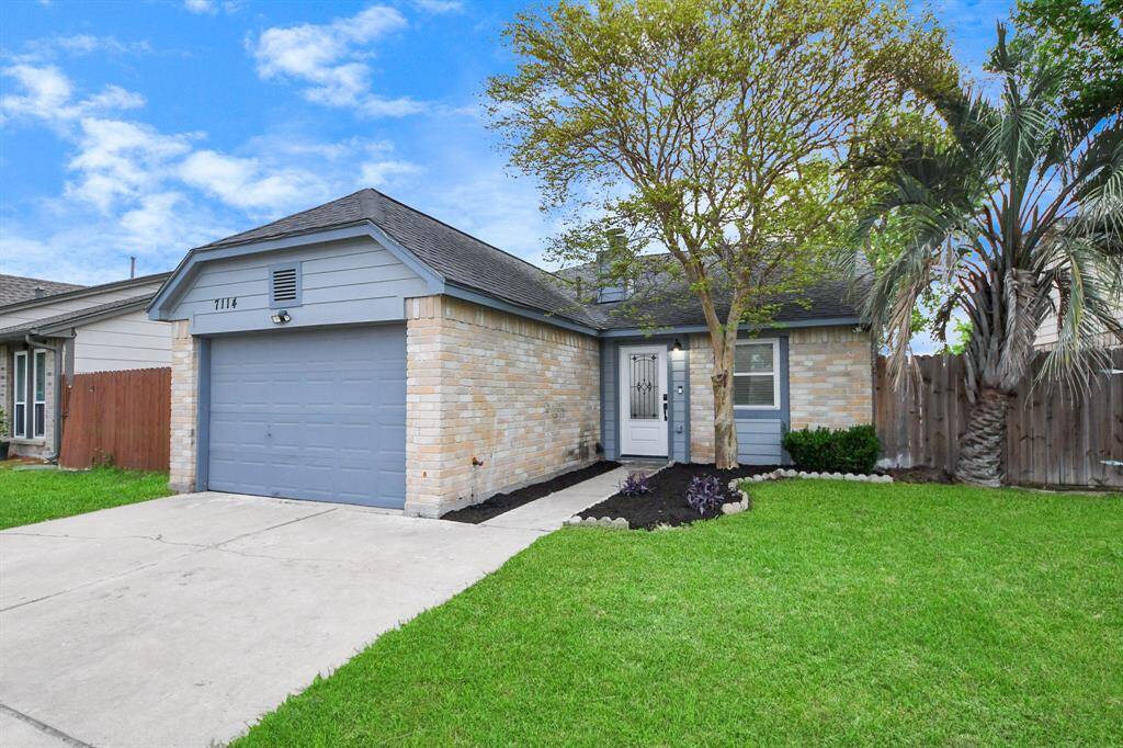 Charming single-story home with a brick exterior and attached garage. Features a well-maintained front yard with a tree and landscaped path leading to the entrance. Ideal for comfortable living with privacy from a wooden fence.