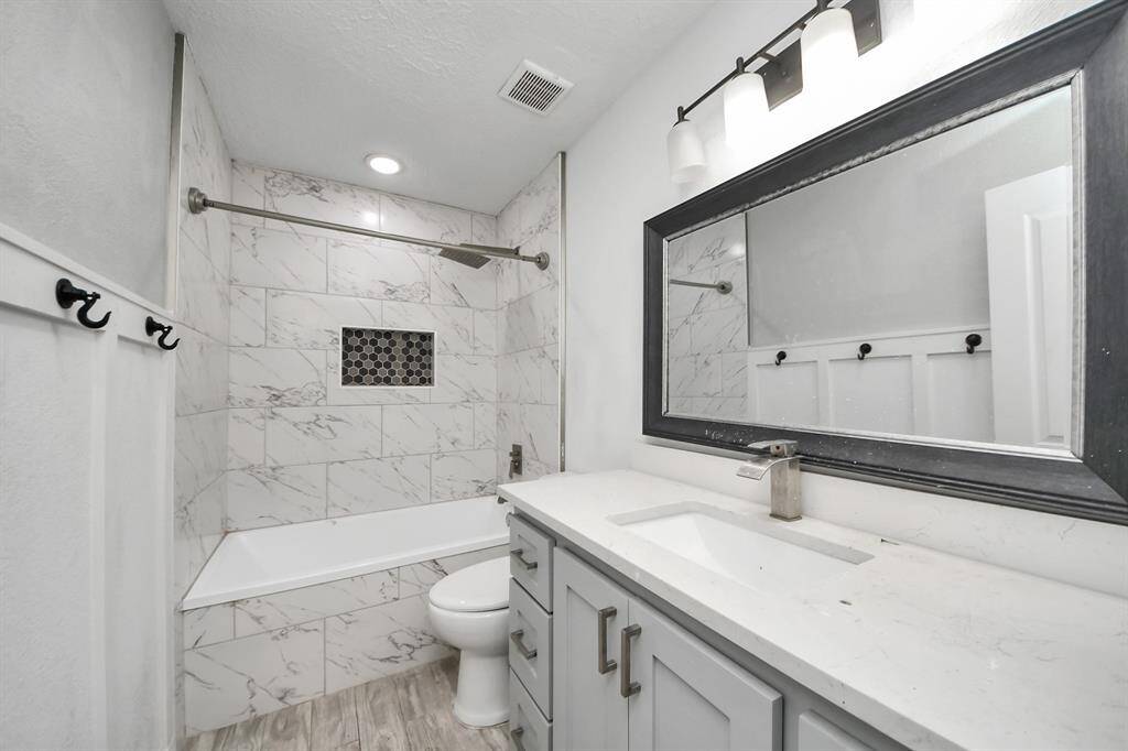 Modern bathroom with elegant marble tile, featuring a spacious tub-shower combo. It includes a sleek vanity with ample storage, a large framed mirror, and contemporary lighting, creating a bright and stylish space.