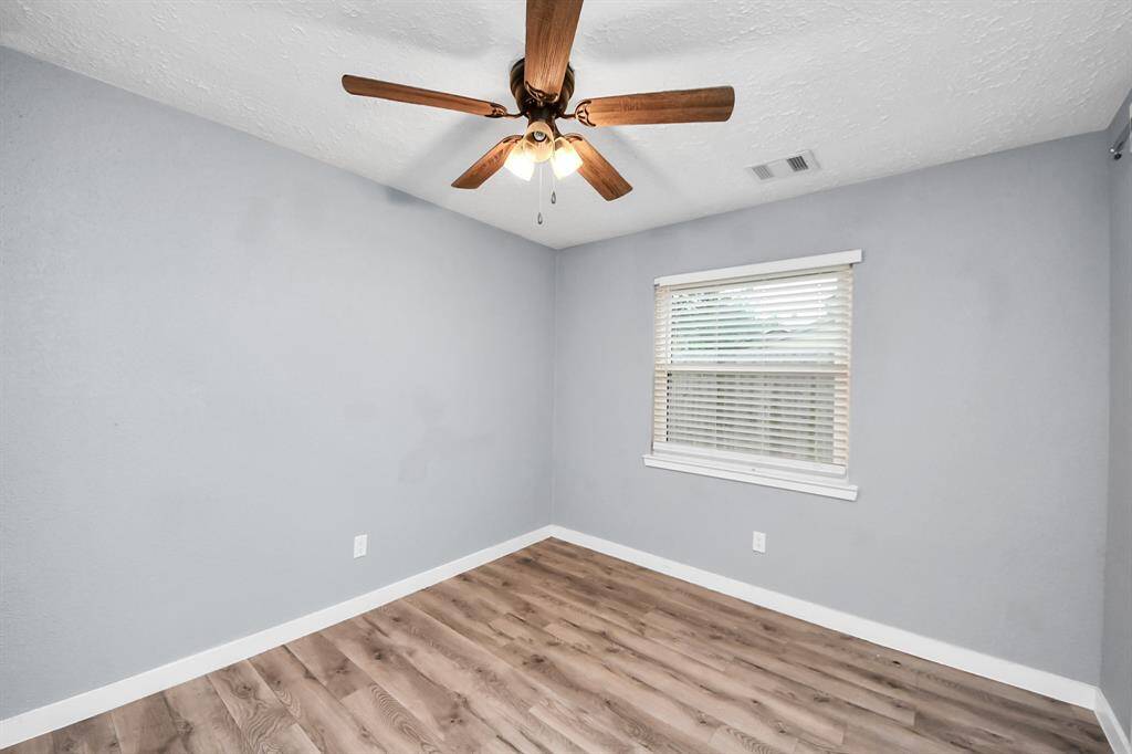 This room features a fresh, light blue color scheme with wood laminate flooring, a ceiling fan, and a window with blinds, providing a bright and airy feel.