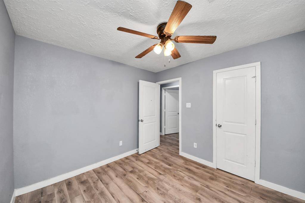 A small room with light gray walls, wood flooring, and a ceiling fan with wooden blades. It features white doors and trim, creating a clean and modern look.