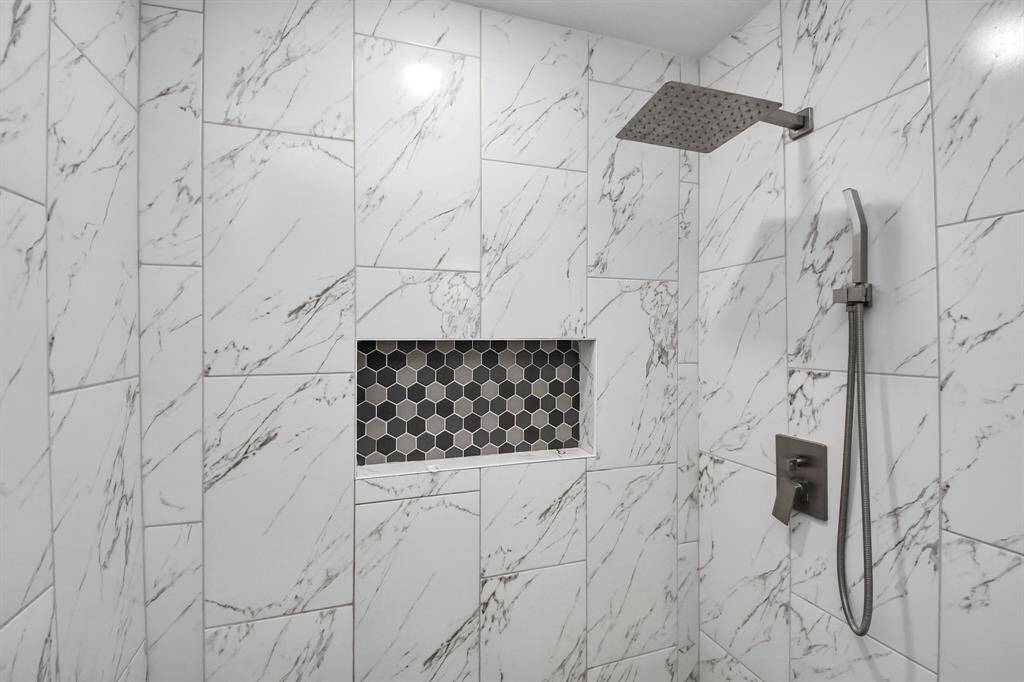 Modern shower with elegant marble-patterned tiles, a rainfall showerhead, and a built-in hexagonal tile niche for storage.