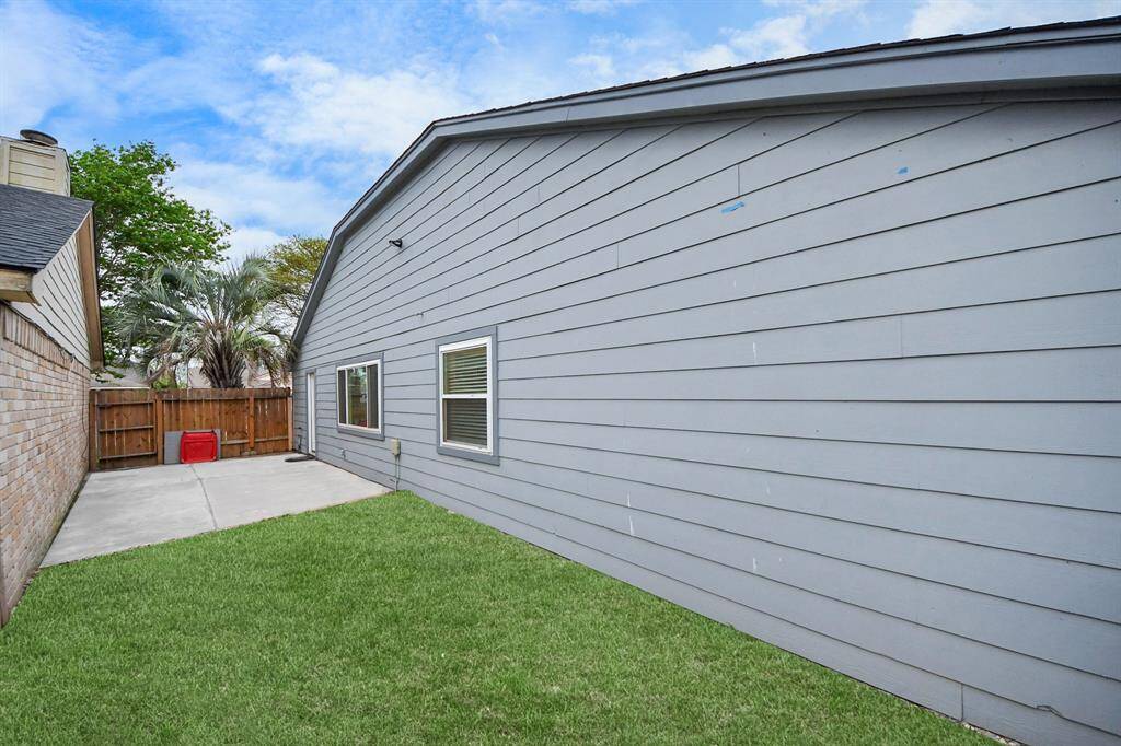 This photo showcases a side yard with a clean, modern exterior and well-maintained lawn. It features a paved walkway, wooden fence, and mature trees for added privacy.