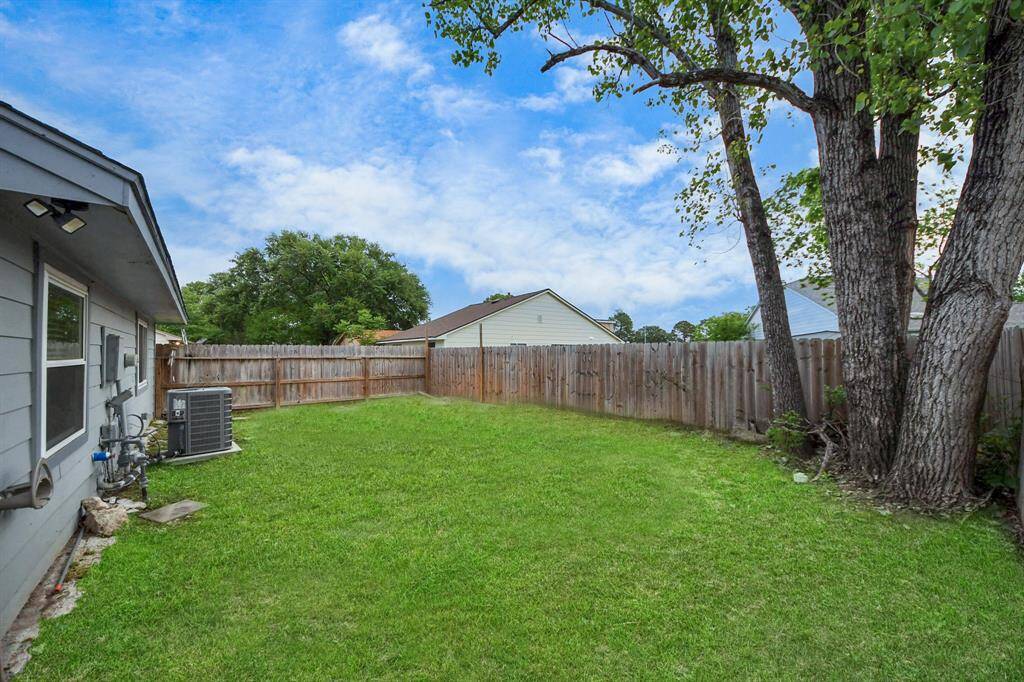 Spacious backyard with well-maintained grass, featuring a large tree and wooden privacy fence. Ideal for outdoor activities and relaxation.