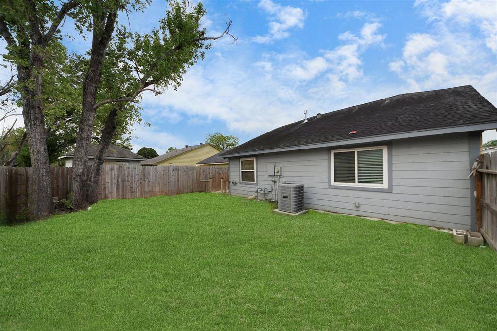 Spacious backyard with well-maintained lawn, mature trees, and a wooden fence for privacy. The back of the house has a clean exterior with large windows and an HVAC unit. Ideal for outdoor activities and relaxation.