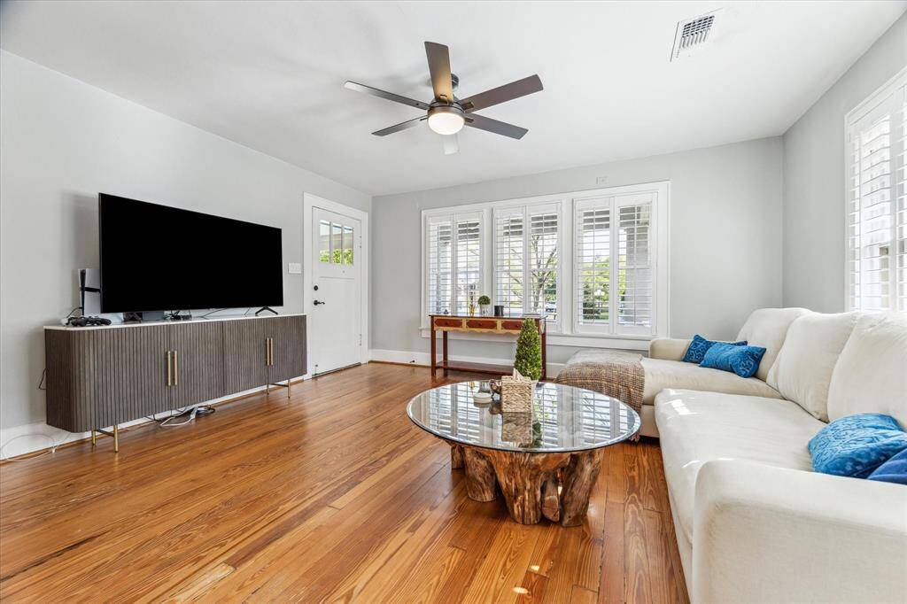 Living room with hardwood floors, ceiling fan with light and window coverings.