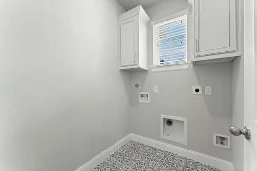 Laundry room with light gray walls, patterned tile flooring, and white cabinetry. It features hookups for a washer and dryer and a small window for natural light.