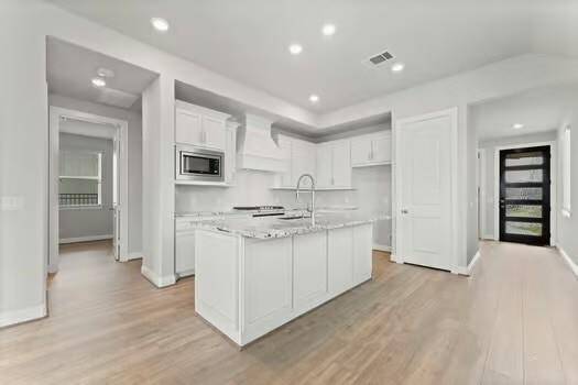 This modern kitchen features sleek white cabinetry, a central island with a granite countertop, and stainless steel appliances.