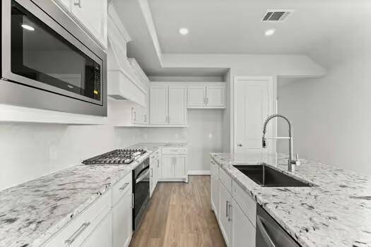 Modern kitchen with sleek white cabinetry, marbled countertops, and stainless steel appliances. Features a built-in microwave, gas stove, and a spacious island with a sink.