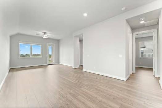 This bright living space features modern, light-colored flooring and walls, a ceiling fan, and large windows that offer plenty of natural light. There's a door leading to the covered patio, and the open layout provides a spacious feel.