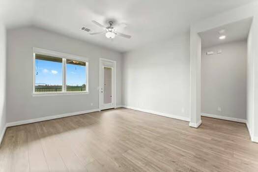 Open and airy living area with light wood flooring, large window, and ceiling fan. Features a neutral color palette and an open layout, perfect for personalization.
