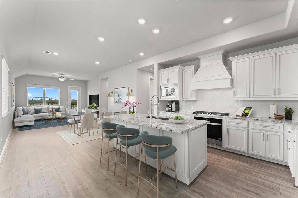Open-concept living space features a modern kitchen with white cabinetry, a large island with bar seating, and stainless steel appliances.