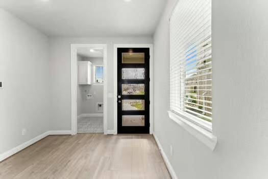Bright entryway with modern wood flooring and a stylish black door featuring frosted glass panels.