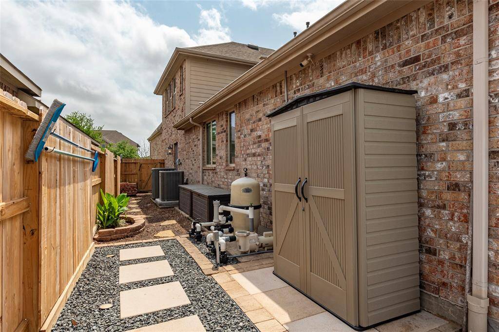 Side yard showcases a clean, well-organized space with professionally-installed hardscape including pavers, rock and stone decking.  The Retractable garden hose reel and water hose mounted outside garage conveys in addition to the outside storage shed and 2 deck boxes.