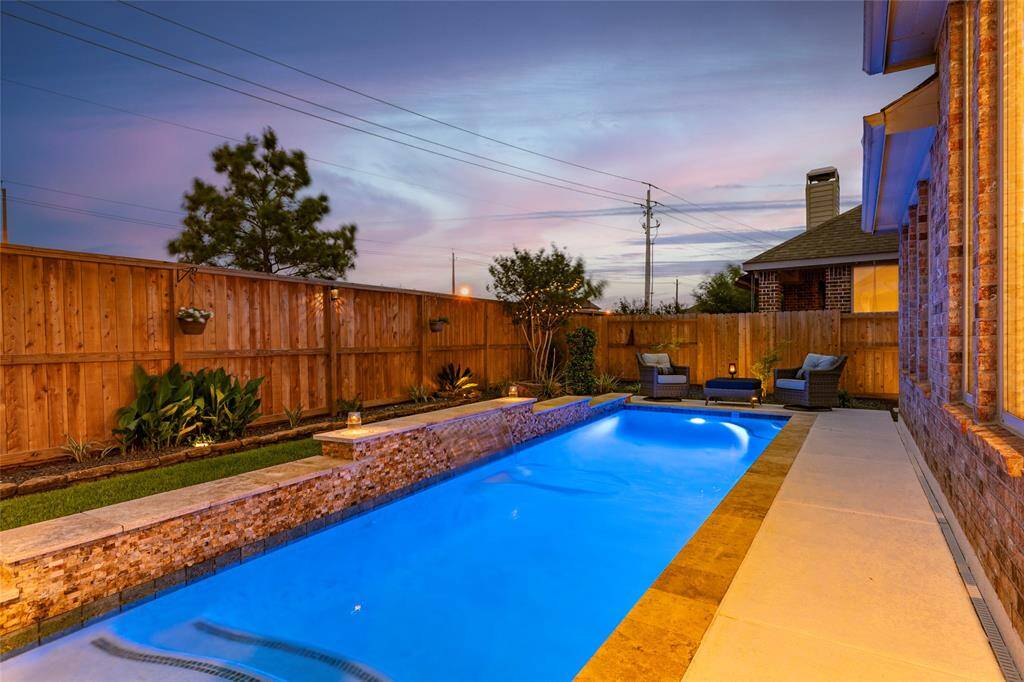Modern backyard with in-ground pool with tanning ledge and water feature, surrounded by Spray Deck patio and split-stone accented water ledge. Backyard showcases easily-maintained and professionally-installed landscape and hardscape including solar-powered lights, extensive pavers, rocks and stone decking throughout. Well-maintained privacy fence and tasteful landscaping are perfect for relaxing or entertaining.