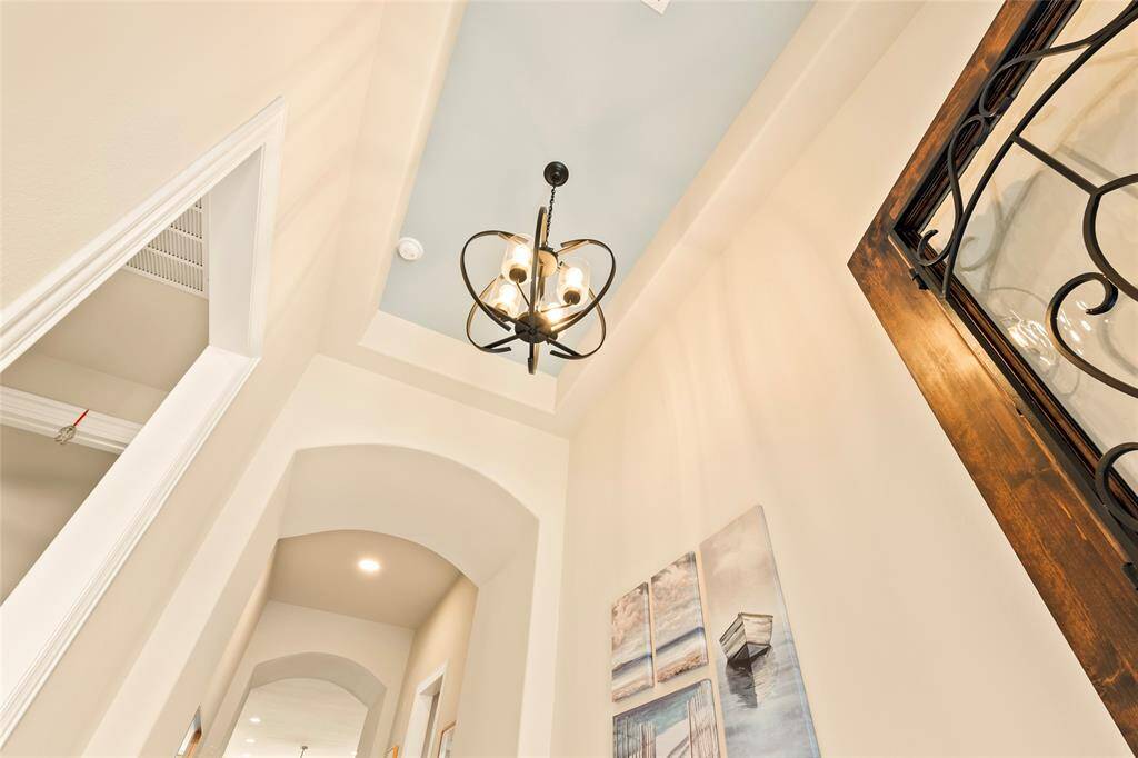 Inviting entrance showcases a high ceilings, updated elegant light fixture and wall art niches. The space includes a stylish wrought iron detail on a front door, adding a touch of sophistication.