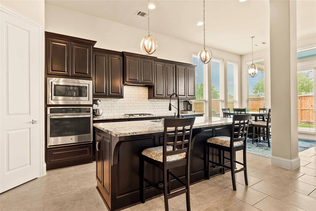 This modern kitchen features slide-out pots & pans drawers in most cabinets for convenience of space. Gorgeous large island with granite countertops, and modern stainless steel appliances. It opens to a bright breakfast area with large windows, offering abundant natural light and a view of the backyard.