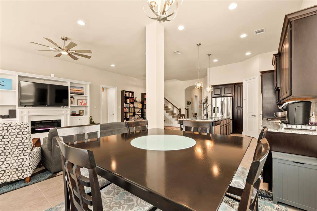 Open-concept breakfast area connects seamlessly to a cozy living area with built-in entertainment center and a fireplace. The room is well-lit with recessed lighting and has a contemporary ceiling fan.