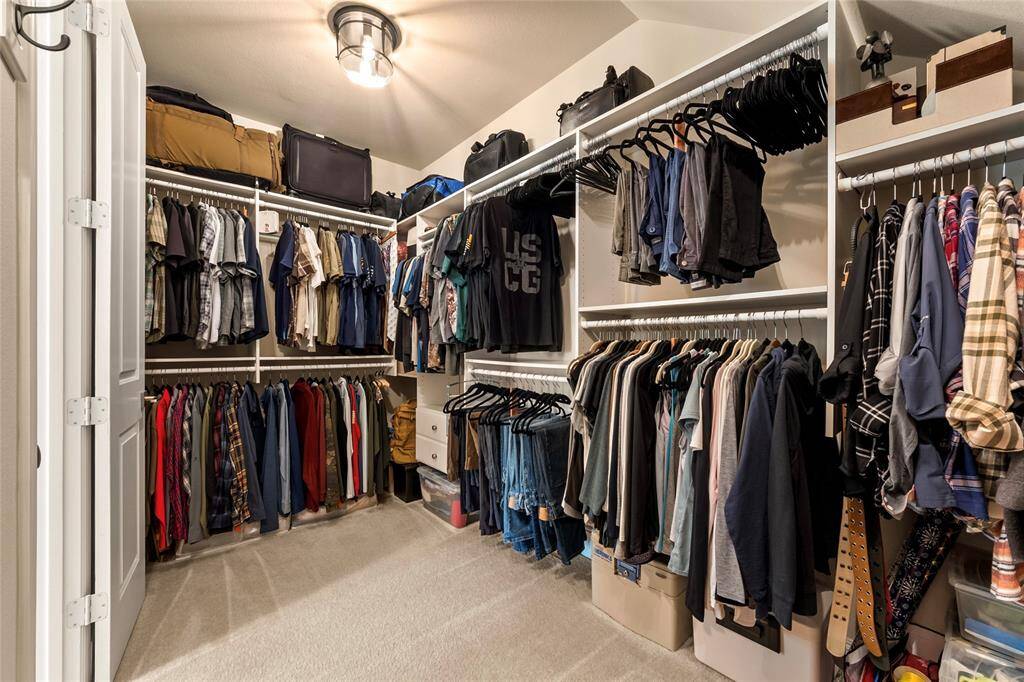 This is a spacious walk-in closet with ample hanging space, shelving, and storage for clothes and accessories. It features carpeted flooring and a ceiling light fixture, offering a well-organized and functional layout.