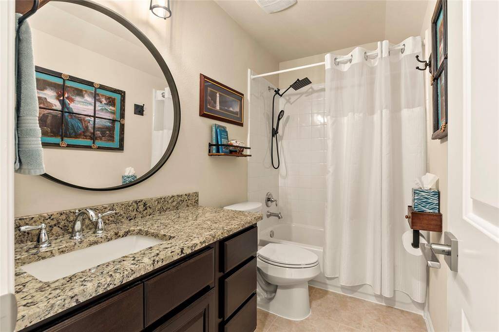 Upstairs full bathroom features a modern design with a granite countertop and dark wood cabinetry. It includes a shower-tub combo with round mirror and bright lighting.