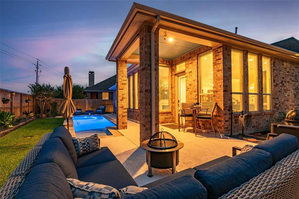 This relaxing backyard features a cozy covered patio with seating area, a sparkling pool with water features and tanning ledge, and durable Spray Decking surrounding, perfect for entertaining.