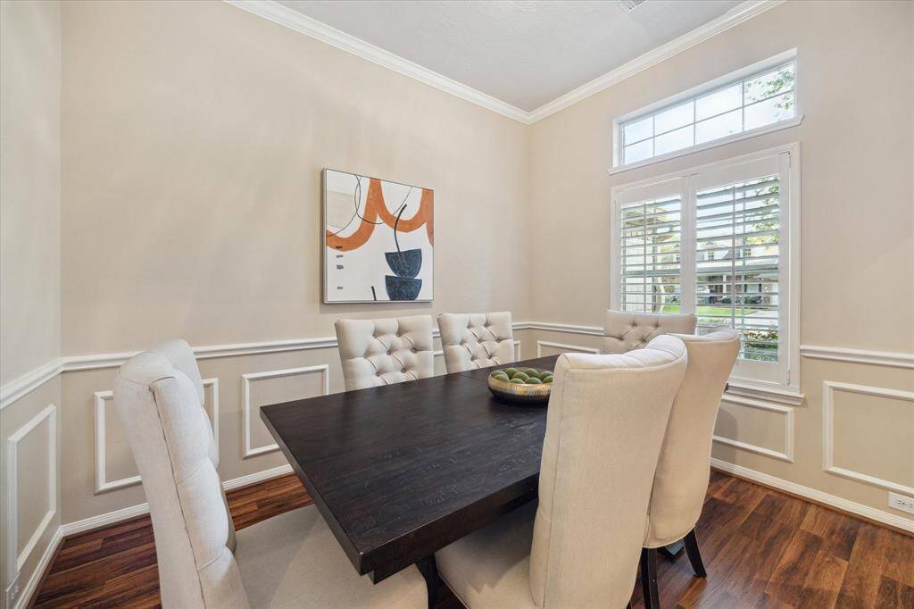 The dining room overlooks the front yard. High ceiling, transom window over large window with plantation shutters, crown molding, and wall trim are elegant features in this airy and bright room.