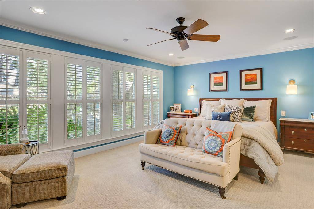 The primary suite features patterned low pile carpet and a wall of windows with plantation shutters overlooking the serene backyard.