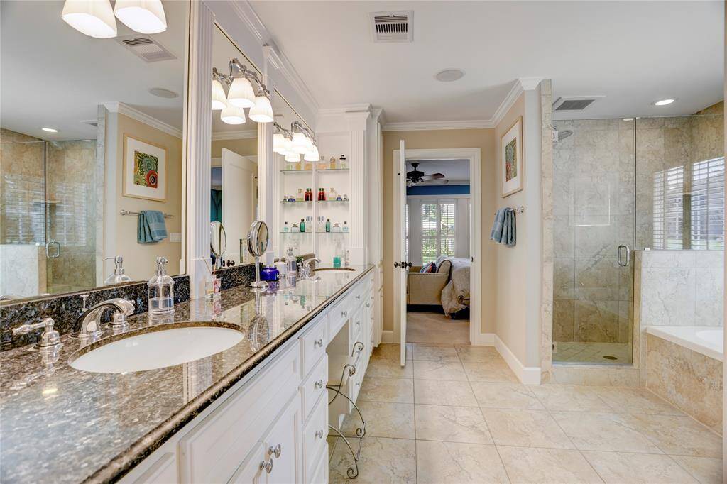 Primary en-suite bath has ample storage, dual sinks, extended vanity, inset glass shelving, custom mirror detailing, frameless glass shower surround and separate soaking tub.