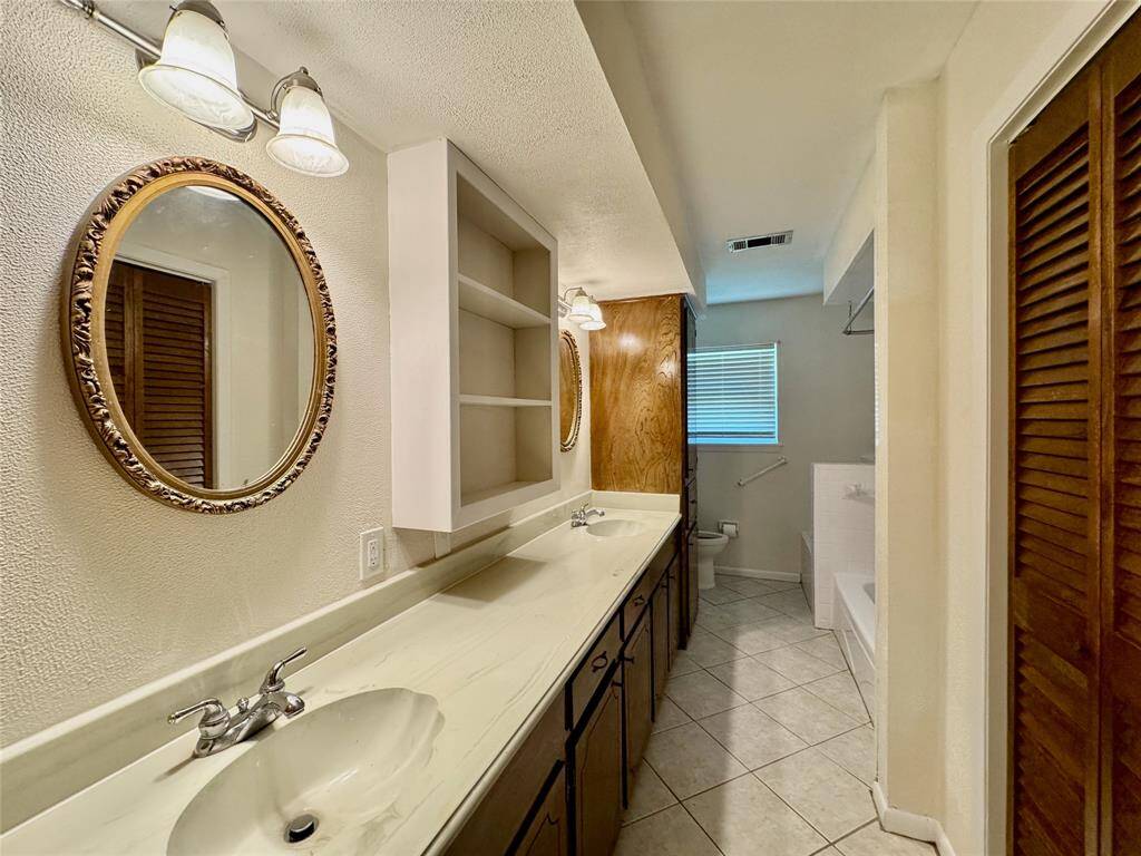 Hallway bathroom features two sinks, long vanity, full tub, commode, and ample storage.