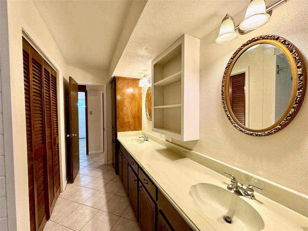 Hallway bathroom features two sinks, long vanity, full tub, commode, and ample storage.