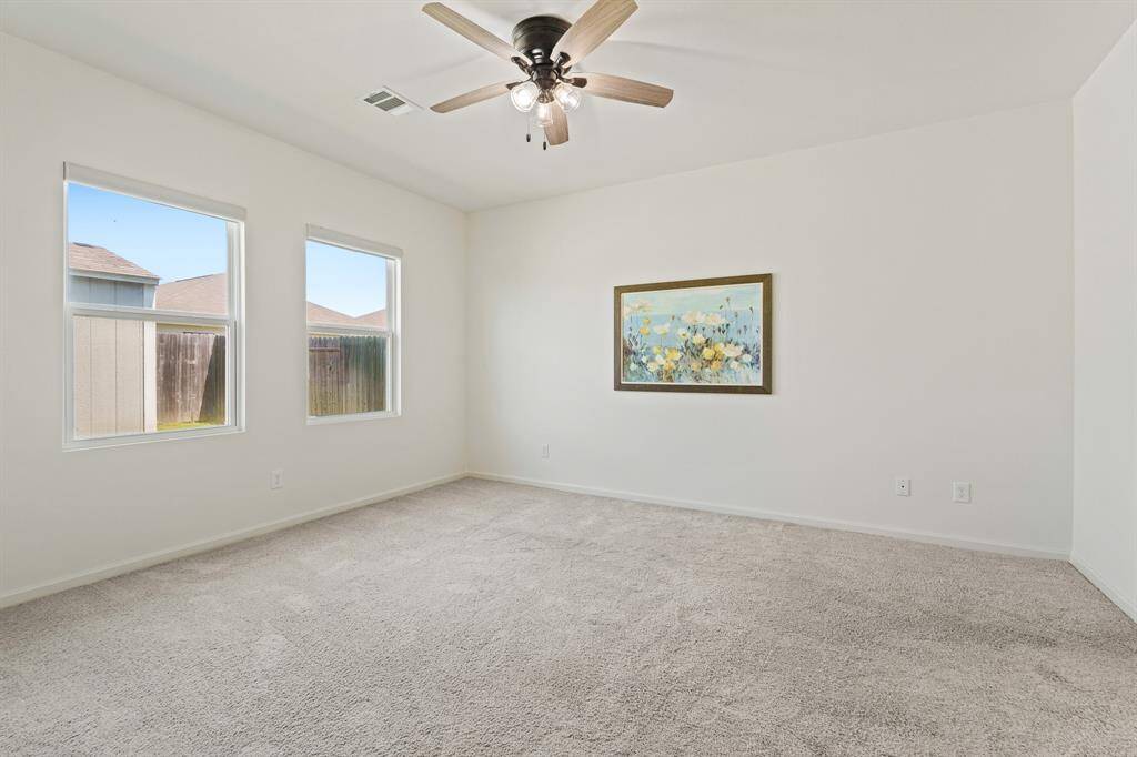 Tucked off the Living Room sits this spacious Primary Bedroom. The room boasts wall-to-wall plush carpeting, two rear facing windows, and a five-blade ceiling fan.