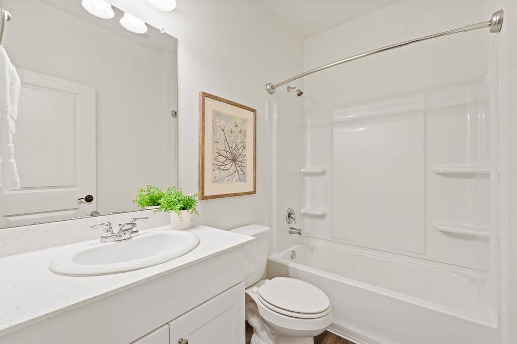 Both Secondary Bedrooms share this centrally located Full Bathroom. The space is finished with the same wood-like flooring, a quartz countertop, undercabinet storage, and a shower/tub combo.