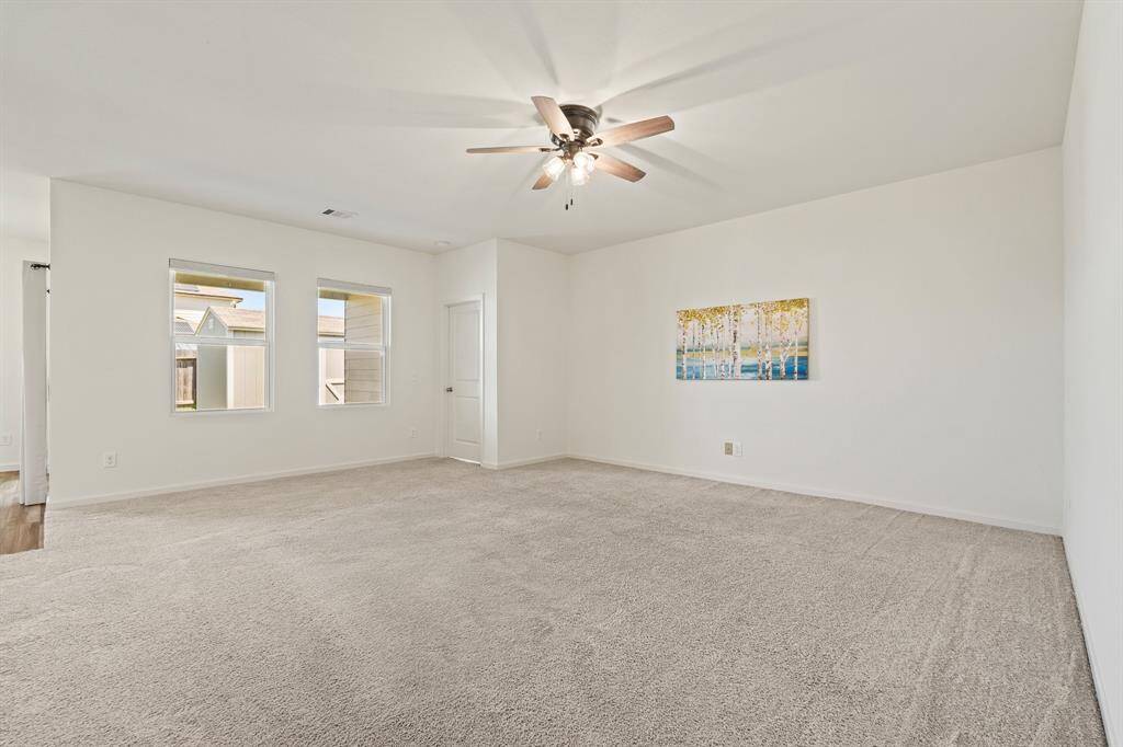 The Living Room boasts plush carpeting, two rear facing windows, and a ceiling fan. The closed door ahead leads to the Primary Bedroom and Bathroom.