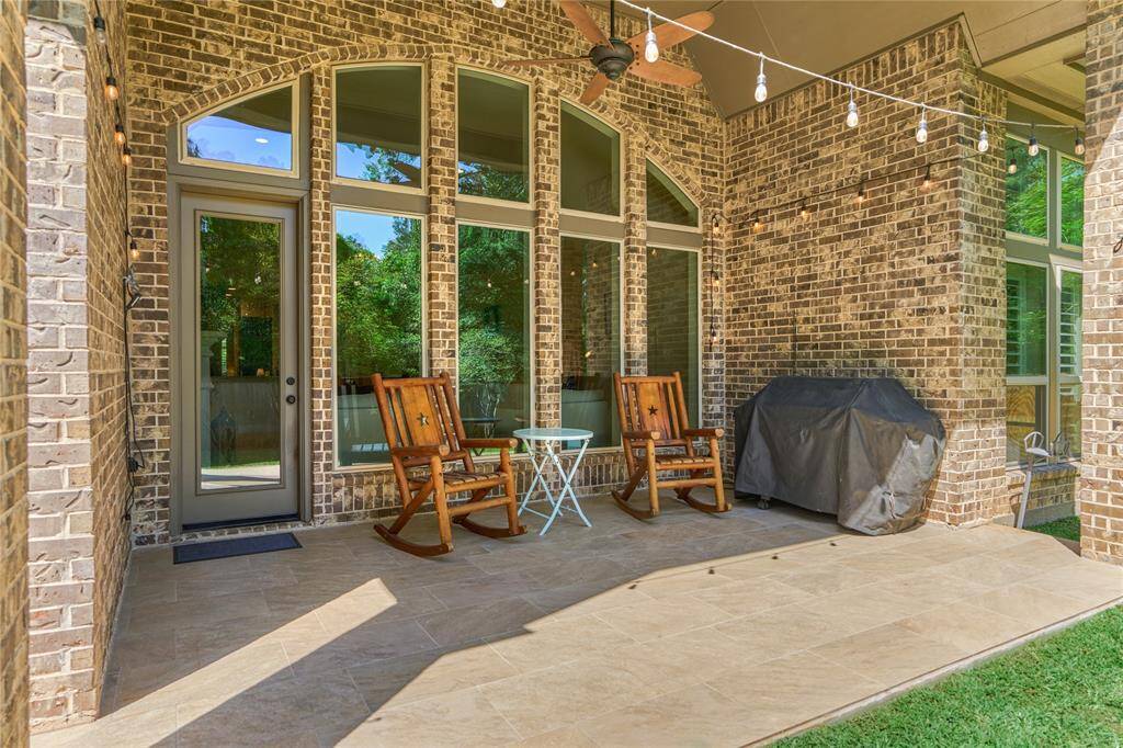 The covered patio has tiled flooring, a ceiling fan, and overlooks the greenbelt.