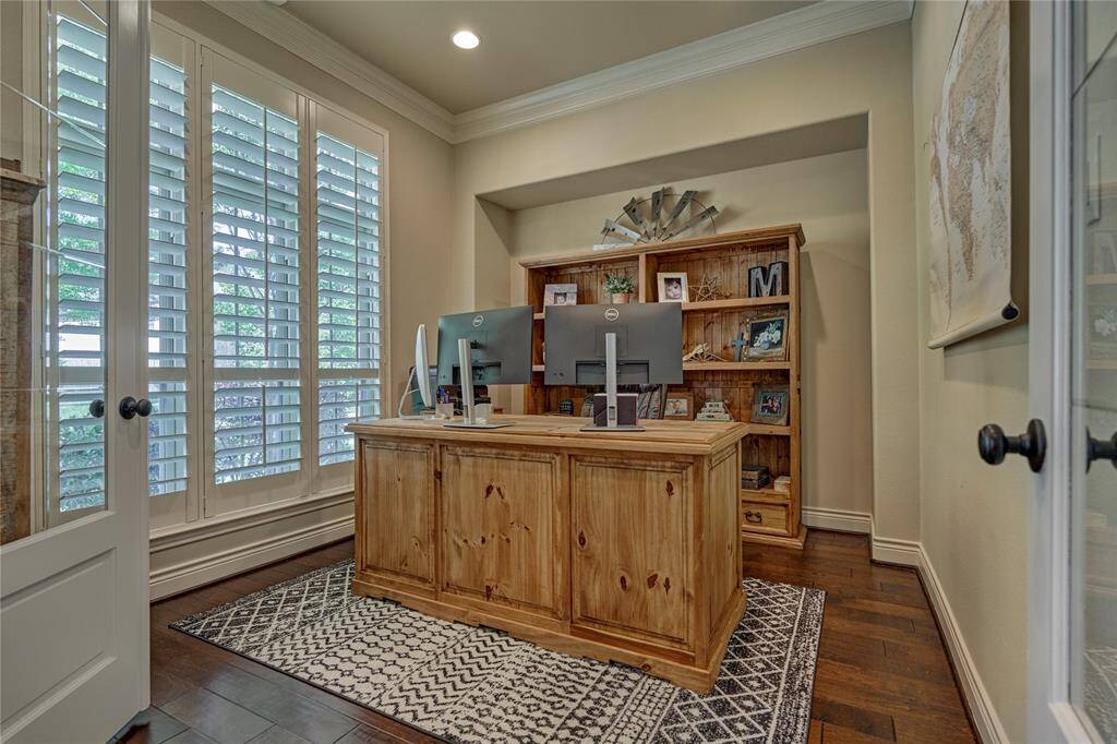 The office features double French doors, elegant crown molding, engineered hardwood flooring, plantation shutters, and a picturesque view of the professionally landscaped front yard.