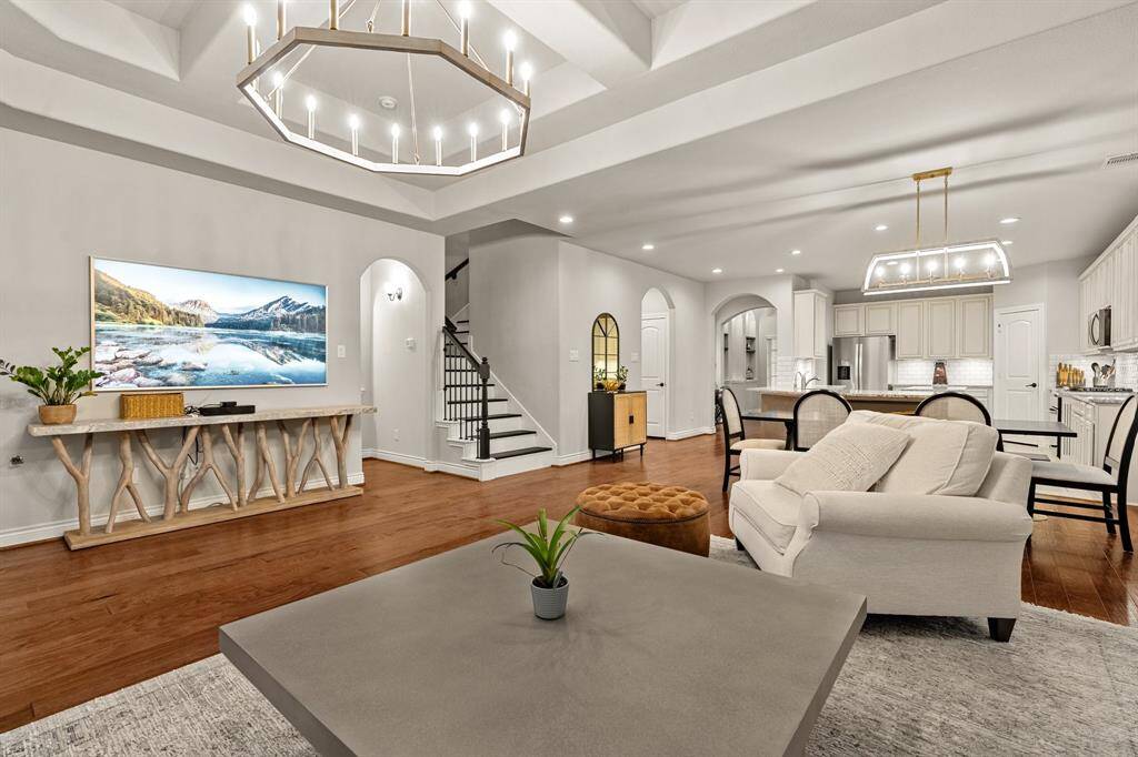 Another view showcasing a spacious open-concept living and dining area with elegant hardwood floors, modern recently upgraded lighting fixtures, and a neutral color palette.