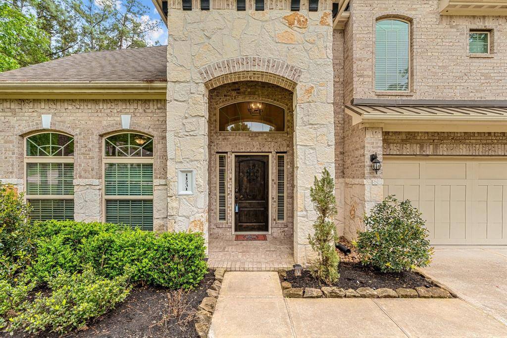 Beautiful two-story brick home surrounded by lush trees and greenery. It features a spacious driveway leading to a three-car garage, a well-maintained lawn, and large windows that suggest plenty of natural light inside.