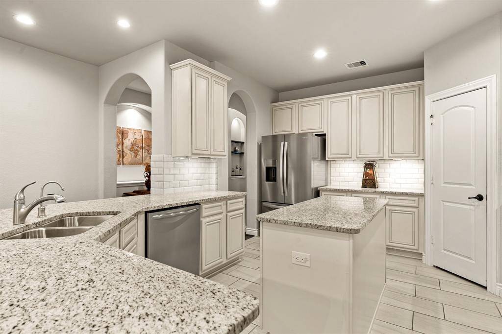 This kitchen features modern stainless steel appliances, granite countertops, and ample cabinet space. The open layout, with arched doorways and subway tile backsplash, adds elegance and functionality.