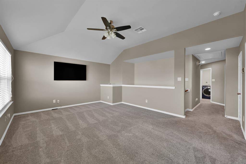 A versatile and open upstairs game room features high ceilings, a ceiling fan, and an alcove wall cutout for extra design flow.