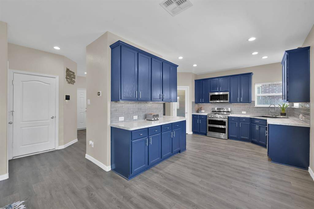 This beautifully updated kitchen features striking navy cabinetry, stainless steel appliances, and a timeless subway tile backsplash.
