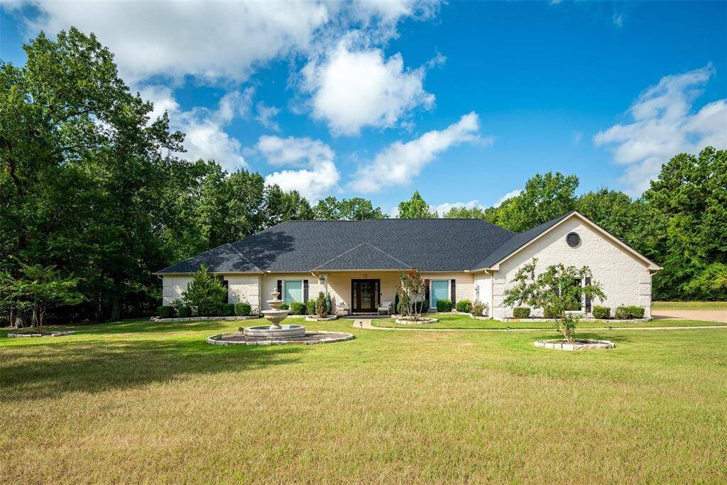 A spacious single-story home set on a large, well-maintained lawn, landscaped garden beds, surrounded by mature trees, offering a serene and private setting.