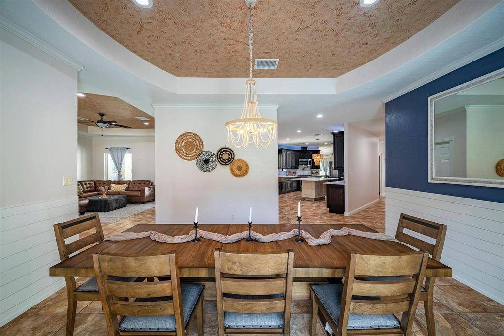 This inviting open-concept space features a dining area with a wooden table, stylish lighting, and decorative wall accents. It seamlessly connects to a cozy living room with a ceiling fan and a modern kitchen with dark cabinets and stainless steel appliances. The design blends warmth and functionality.