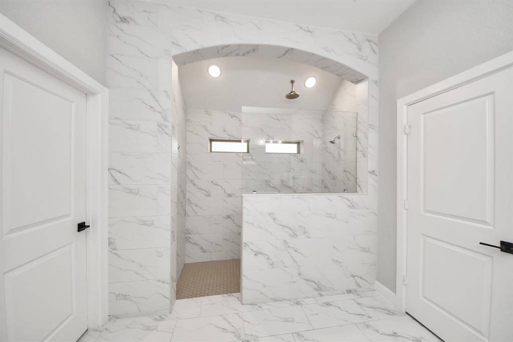 This bathroom features a spacious, well design elegant marble-look tiles and a walk-in shower. The glass partition and overhead shower add a luxurious touch.