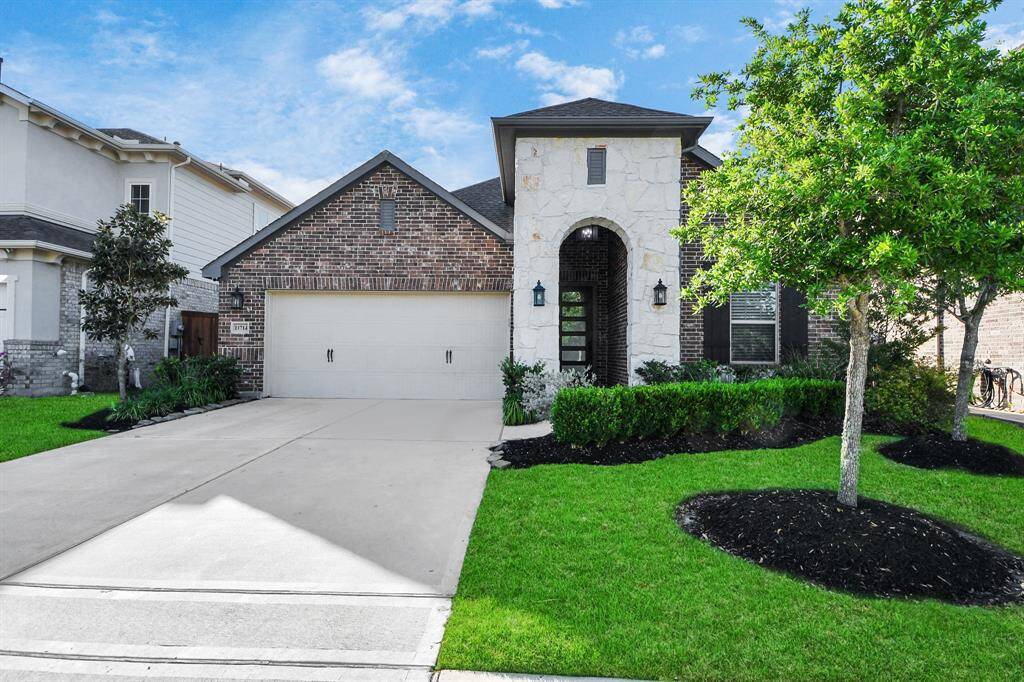 Single-story home with a brick and stone facade, featuring a two-car garage. The property offers well-maintained landscaping, lush green lawn, and inviting curb appeal in a peaceful suburban setting.