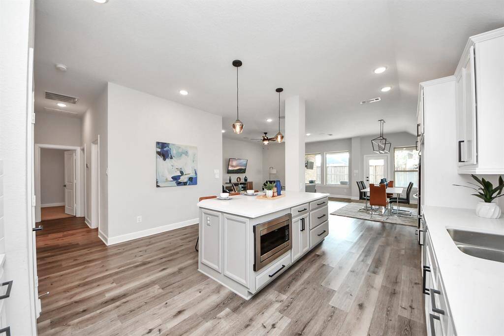 Kitchen features an open layout, a large island with microwave. It seamlessly connects to a bright dining area with large windows, offering a welcoming and functional space.