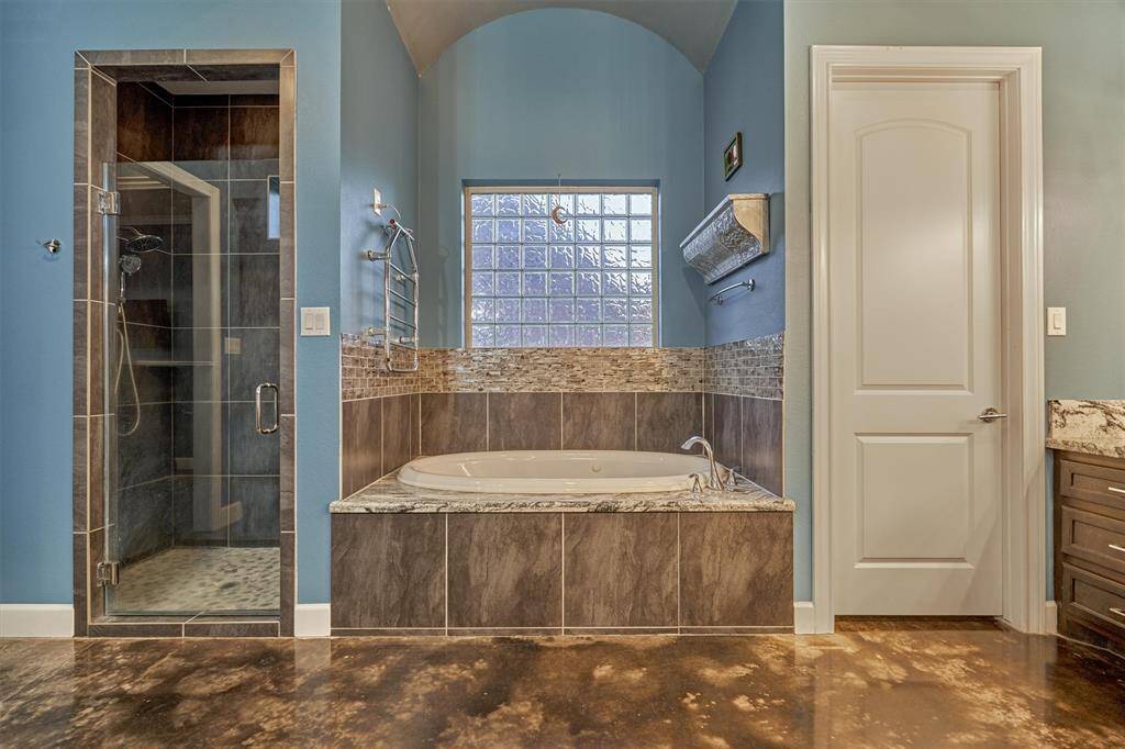 The soaking tub in the primary bath is beautifully accented with glass tile, which is echoed in the shower design for a cohesive, upscale look. A heated towel bar above the tub adds a luxurious touch, keeping towels warm and cozy.