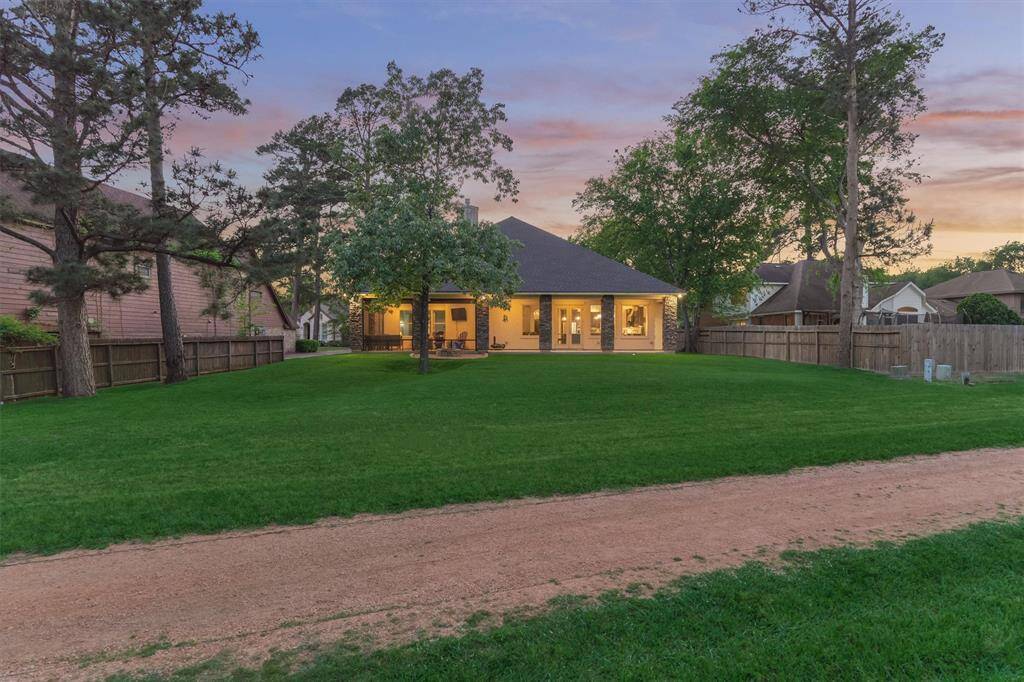 A nighttime view of the back of the home showcases the beautifully lit exterior, expansive yard, and direct access to the scenic walking trail—creating a peaceful and inviting outdoor retreat.