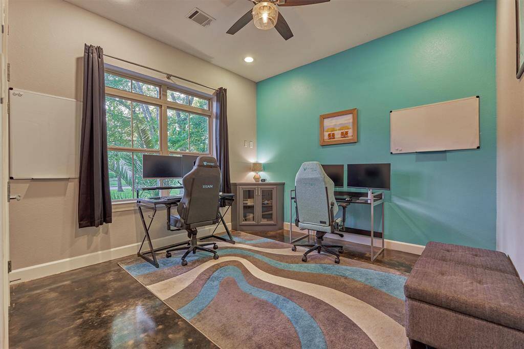 The first guest bedroom, currently used as a home office, features a large window that fills the space with natural light and offers a charming view of the front yard.