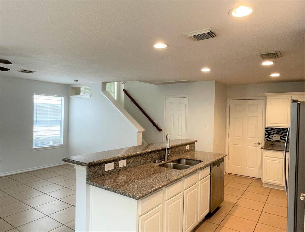 Bright and open kitchen and living area with tile flooring, granite countertops, stainless steel appliances, and a view of the staircase. Ideal for modern living.