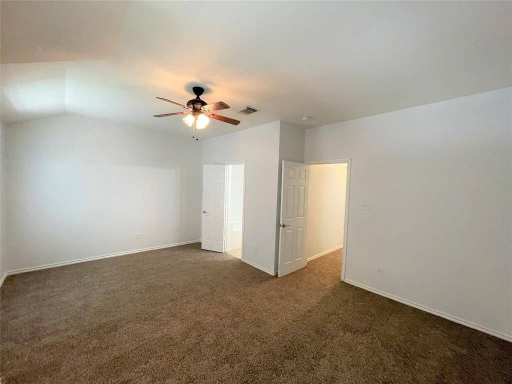This spacious bedroom features neutral walls, cozy carpeted flooring, and a ceiling fan with light. It includes two doors—one leading to a closet and the other to an adjoining bathroom, providing convenience and comfort.